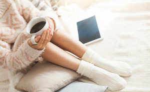 Soft photo of woman on the bed with tablet and cup of coffee in hands, top view point